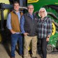 Two men and one woman standing in front of a green tractor