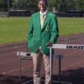 A young man wearing a green 4-H blazer stands smiling on a running track.