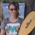 A teen girl smiling, wearing sunglasses and holding a rowing oar.