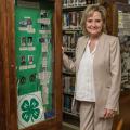 A woman stands in front of library book shelves beside a tall, green 4-H display.