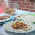 Three plates with tortillas, fish, and a completed grilled fish taco with peach salsa on a picnic table. 
