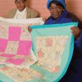 2 women hold up quilts.
