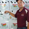 A man wearing a maroon shirt stands in front of a wall of boxes from Eubanks Produce Farm.
