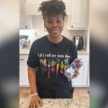 A woman stands in kitchen with a cell phone displaying a web page.