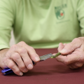 A person wearing a green shirt scraping a stem with a razor bade. 