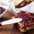 A knife spreading strawberry jam on toast.