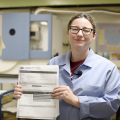 Woman in blue lab coat holding up paper.