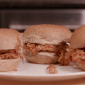 Three small sandwiches made with whole wheat slider buns, shredded chicken, and barbecue sauce on a white plate. 