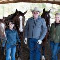 A man and two girls stand in a barn with three horses.