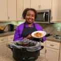 A woman stands in a kitchen and holds a serving of Chicken with Peachy Ginger Sauce.