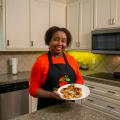 A woman stands in a kitchen holding a plate of salmon patties for the camera.