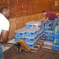 Two men move cases of bottled water in a storehouse.