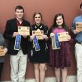 Five people stand in a row holding their awards. 