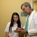 A teenage girl looks on as a doctor explains a chart in his hands.