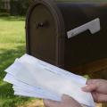 A pair of hands holds a stack of mail taken from a mailbox.