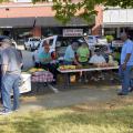 Several people gather to buy produce on display at a farmers market.