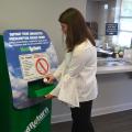 Young woman places a prescription bottle in secure slot in a large, green metal box