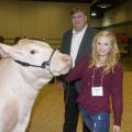 A teenage girl holds the halter on the face of her muscular, white steer as she and a tall man standing behind them look at the photographer.