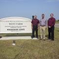 Three men stand beside a white sign on a cloudless day. The sign reads “Delta Research & Extension Center, West Farm, Mississippi Agricultural and Forestry Experiment Station, Mississippi State University.”