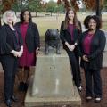 Four women stand around the Bully statue on the Mississippi State University campus.