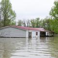 A gray, double-wide manufactured home with flood waters reaching the lower windows and surrounding area