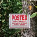 A private property sign is nailed to a tree with vegetation in the background.