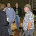 A man in a gardening hat stands and talks to three adults, with several others milling about in the background.