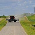 A red combine drives down a gravel road with farmland on both sides.