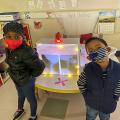 Two children in masks stand in front of an activity center in a classroom.