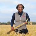 A woman holds a stalk of grain while standing in a field.