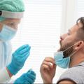 Medical worker in protective clothing takes a throat swab from a male patient.