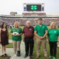 Five people pose for a photo on a football field.