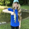 Girl in a blue T-shirt and baseball cap holding a small fish.
