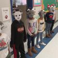 Six children stand in a hallway wearing paper masks depicting billy goats.