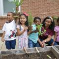Four students stand in a row with their teacher and hold up the herbs they were about to plant in the raised bed.