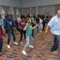 Man leads room full of teenagers in dance exercise.