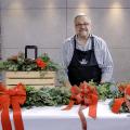 A man stands in a studio with a completed velvet bow, garland, door swag, and table centerpiece.