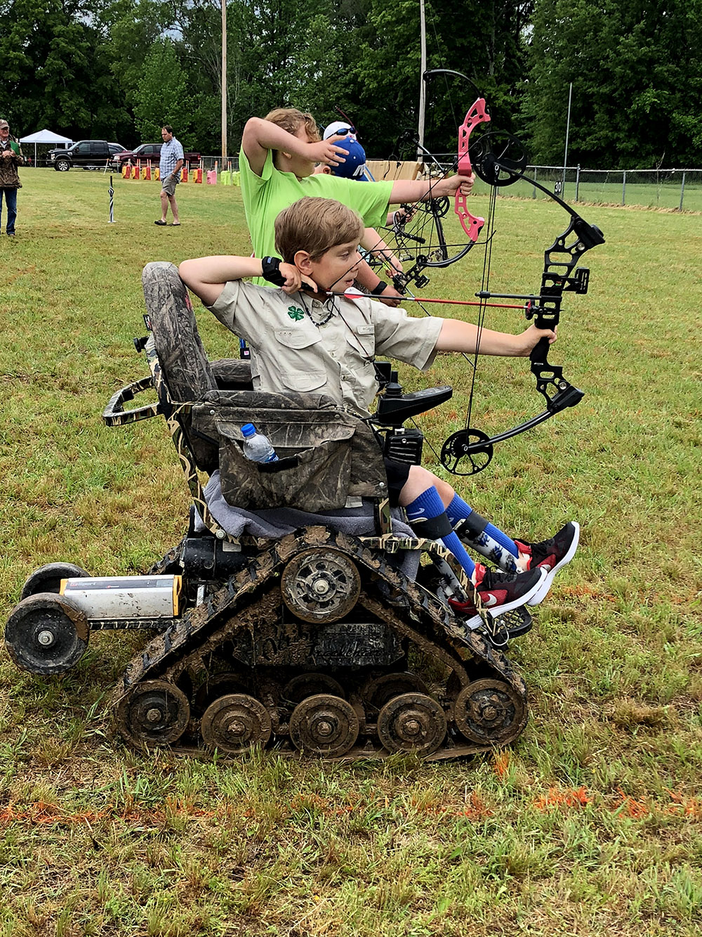 A teenager aiming his bow and arrow from his wheelchair.