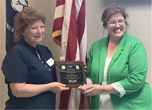 Two women hold a plaque in front of the American flag