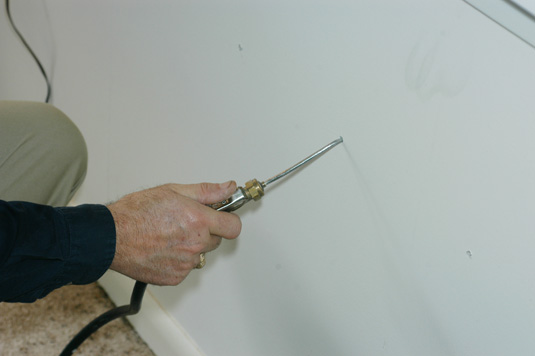 Termiticide foam is being injected into a wall void. The foam has a consistency similar to shaving cream.